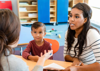 Parental rights concept. Mother speaking with teacher in school. A woman and a young boy sit across from another woman at a table, engaged in conversation in a classroom setting. The boy looks curious while the women appear to be discussing something important.