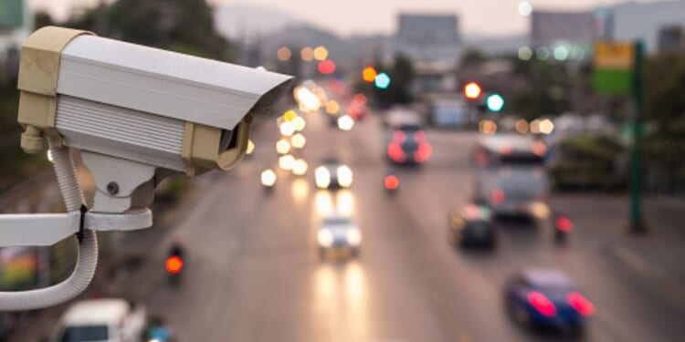 A traffic surveillance camera is pictured above a street at dusk.