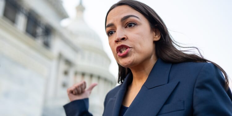 A woman in a navy blazer gestures and speaks emphatically about the alleged hoax in front of a government building with a dome, possibly the U.S. Capitol, during the daytime.
