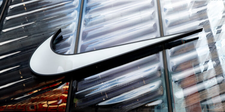 A large white Nike swoosh logo is displayed on a glass building facade, reflecting light and surrounding structures.