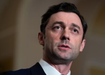 Senator Jon Ossoff is pictured in a suit and speaks, looking slightly to the side, with a neutral background and soft lighting focused on his face.