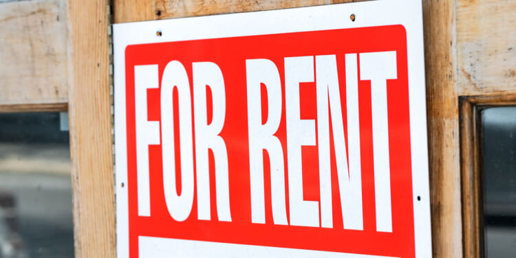 A close-up of a red and white For Rent sign is attached to a wooden door, indicating that the property is available for leasing.