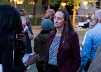 A woman in a maroon blazer listens to a person in a black top during an outdoor gathering in Seattle, with several people talking in the background.