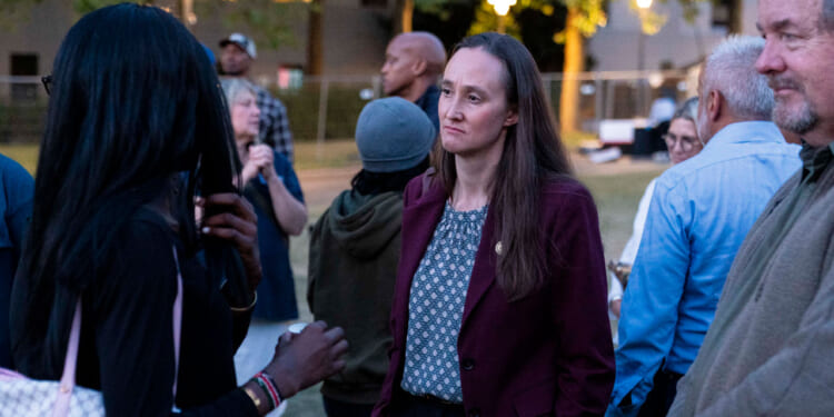 A woman in a maroon blazer listens to a person in a black top during an outdoor gathering in Seattle, with several people talking in the background.