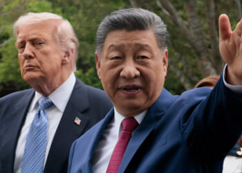 Donald Trump and Xi Jinping in suits stand outdoors; Xi gestures with his hand while the Trump looks on with a serious expression. Trees and greenery are visible in the blurred background.