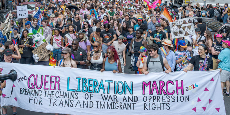 Transgender activists at a march. Pictured: a diverse crowd marches, holding a banner reading Queer Liberation March: Breaking the Chains of War and Oppression for Trans and Immigrant Rights amid colorful signs and pride flags.