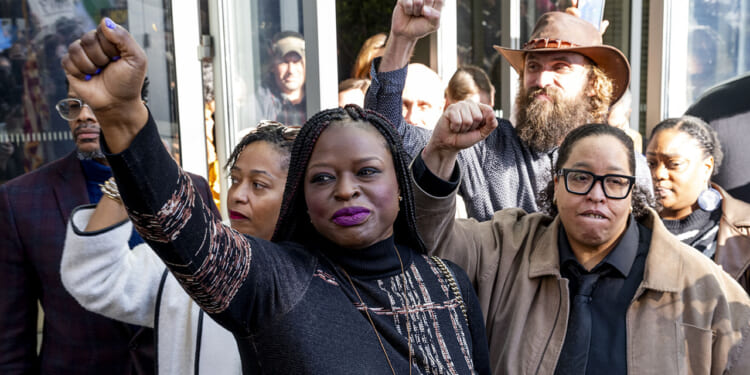 Nekima Levy Armstrong and others who invaded Cities Church. A group of people stand together with raised fists, showing solidarity. The central figure, a woman in a patterned top, looks determined. Others around her also have fists raised and appear resolute.