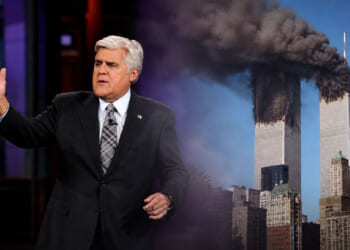 Jay Leno in a suit gestures while speaking, with the burning Twin Towers of the World Trade Center in the background under a blue sky on 9/11.
