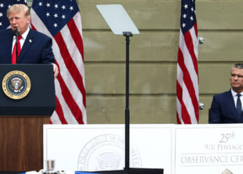 Donald Trump speaks at a podium with the U.S. presidential seal, while Pete Hegseth sits nearby. American flags are in the background, and a sign reads 25th 9/11 Pentagon Observance Ceremony. The event highlights ongoing discussions of national security, including concerns about countries such as Iran.
