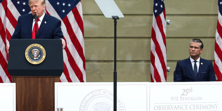 Donald Trump speaks at a podium with the U.S. presidential seal, while Pete Hegseth sits nearby. American flags are in the background, and a sign reads 25th 9/11 Pentagon Observance Ceremony. The event highlights ongoing discussions of national security, including concerns about countries such as Iran.