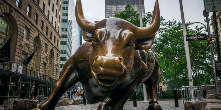 A close-up view of the Charging Bull bronze sculpture in New York Citys Financial District, with buildings and street signs visible in the background.