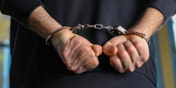 A man is pictured handcuffed in a dark blue shirt.