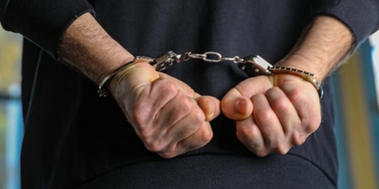 A man is pictured handcuffed in a dark blue shirt.