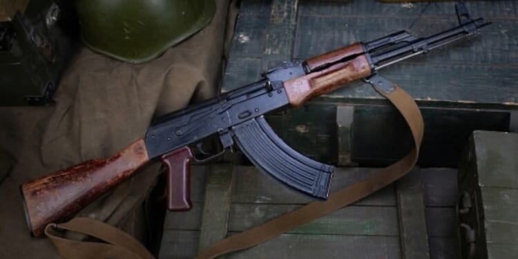 An AK-47 rifle lays on a military box above ammunition.